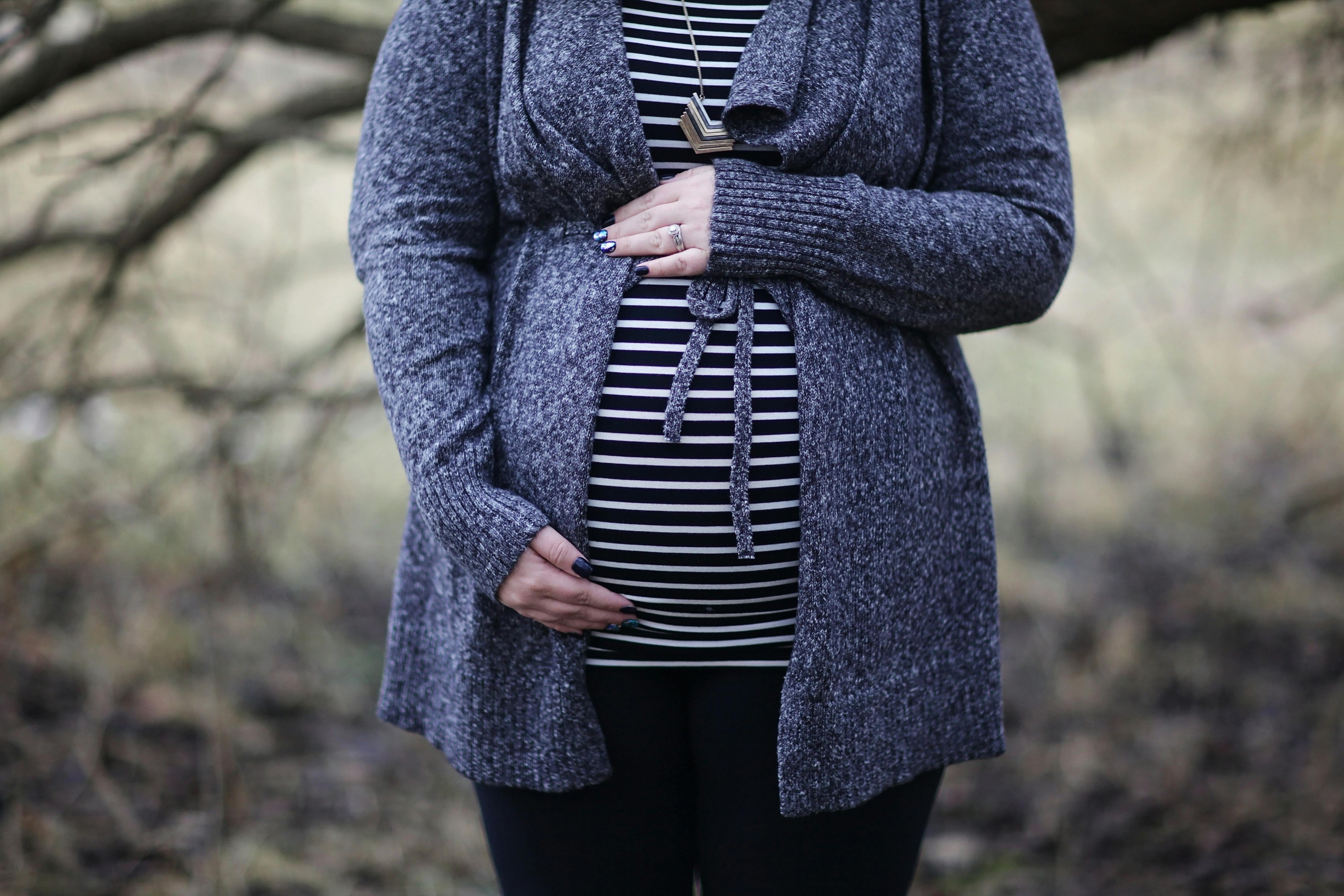A pregnant woman standing in the park. 
