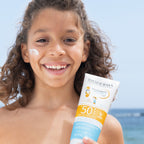 Child holding a Bioderma sunscreen tube with a beach background