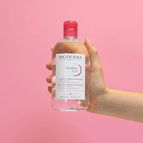 Hand holding a Bioderma Sensibio H2O bottle against a pink background