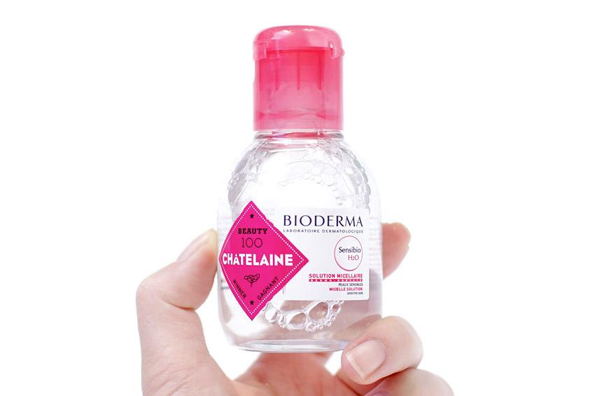 Hand holding a Bioderma bottle with a pink cap on a white background