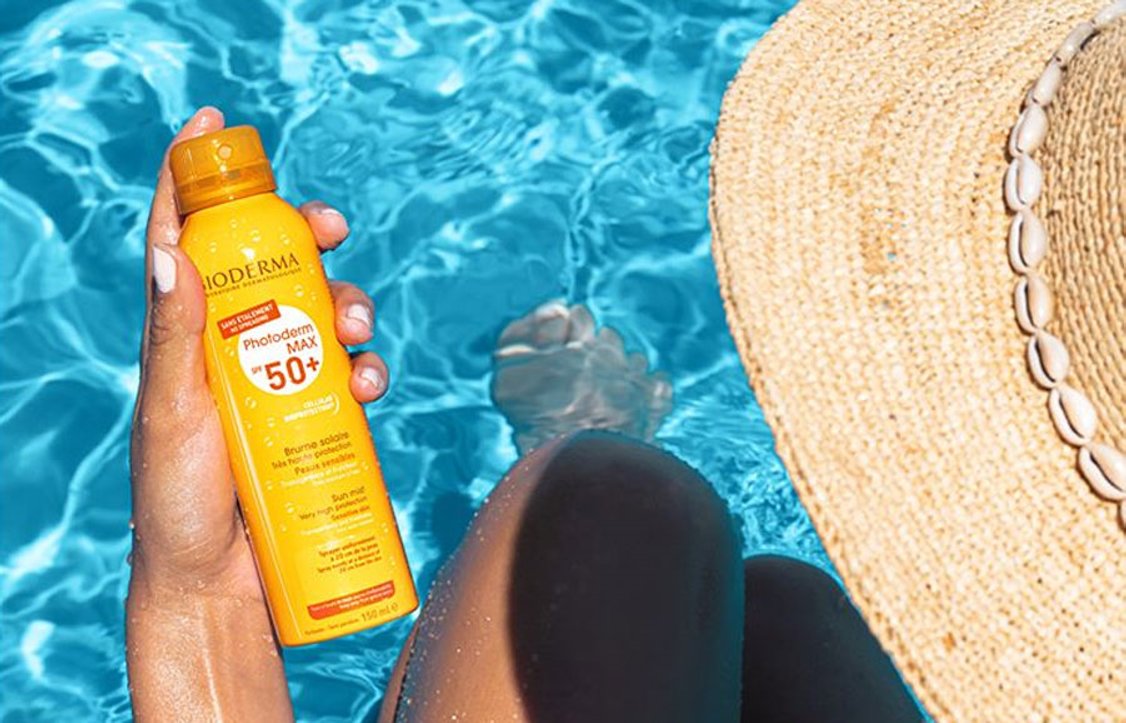 Person holding a Bioderma sun spray by a pool