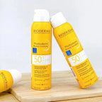Two bottles of Bioderma Photoderm Brume Invisible sunscreen on a wooden surface with a white background.