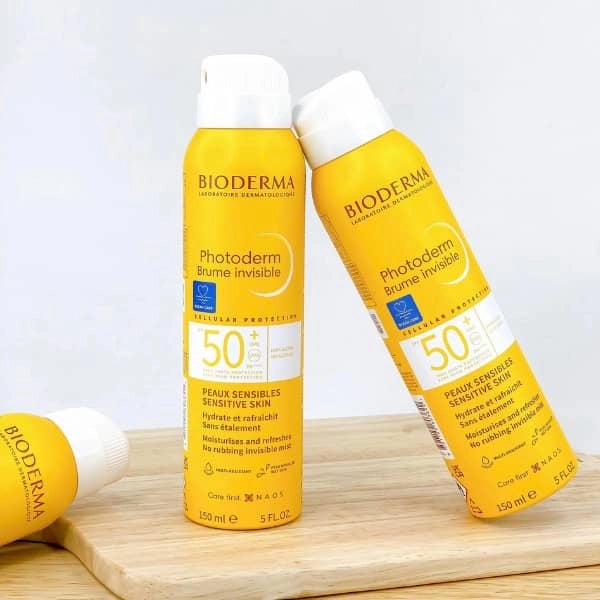 Two bottles of Bioderma Photoderm Brume Invisible sunscreen on a wooden surface with a white background.